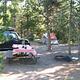 A picnic table, fire pit, car parked and tent pitched under pine trees at Indian Creek Campground