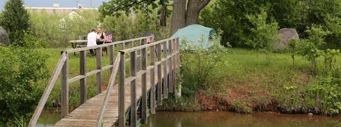 Footbridge over water with picnic table and a tent visible — shows campsite access, tent camping and campsite setting.