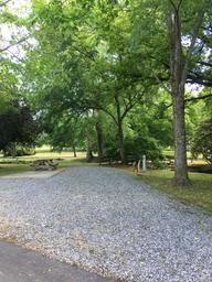 Gravel RV/campsite with picnic table, utility pedestal and mature trees — clearly a site photo from the ‘Sites’ page (shows typical pitch and setting).
