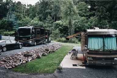 Two motorhomes parked on landscaped pads with gravel and surrounding woods — clear view of full‑service RV parking and site spacing (from Rates page imagery).