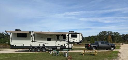 Ground-level photo showing an RV and tow vehicle on a full-hookup site with picnic table and open lot — good campsite detail; comes from the McAlpin page hero image.