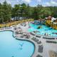 Aerial view of the campground’s large resort-style pool and water play area with surrounding deck chairs and nearby woods/lake — good overall overview of a key on-site amenity (image appears on the property homepage/gallery).