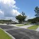 Ground-level view of paved road and pull-thru/back-in gravel pads with waterfront sites and picnic tables — useful for showing individual site setup (Site 15 / RV lodging image).