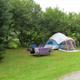 Tent campsite on a grassy, treed site with picnic table and fire ring — representative image of tent camping options on the campground (from 'ways to stay' page images).