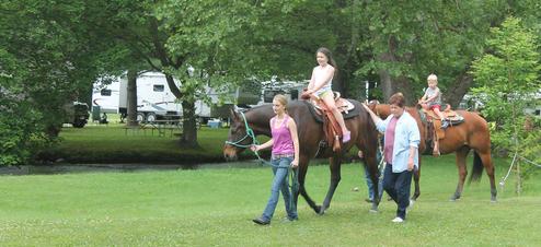Image of horseback riding activity with RVs and open campsite area visible in background — demonstrates recreational offerings and campsite layout (slider2 image).