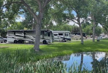 Pull-in RV sites shown on grass with a small pond/landscaping in foreground — matches images on the 'Ways to stay' pages and highlights level pull-in sites and scenery.
