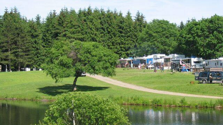 Wide view across a pond to grassy campground area with RVs and hookups visible — useful scenic/site photo (homepage image).