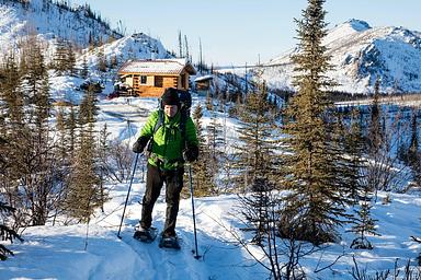 A man snowshoes from a log cabin