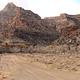 Tan sandstone cliffs rise up behind a gravel road with a campsite on one side and bare cottonwood trees on the other.