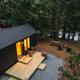 Aerial/angled exterior view of a tiny cabin on a riverside, showing deck, picnic table and firepit — good overview of waterfront lodging and site layout on the Camp Hudson Pines homepage.