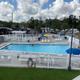 Clear on-site photo of the campground pool area with surrounding deck, lounge chairs and RVs visible in the background — useful facility image shown on the property’s hero/activities sections.