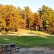 Open grassy campsite area with picnic table and a cabin in the tree line during fall colors — good view of cabin/rental and grounds from the campground listing page.