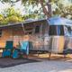 Airstream-style RV parked on a gravel site with shade and outdoor chairs — shows RV pitch accommodations and site setup; sourced from the property gallery.
