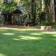 Flat grassy field, horseshoe pit, picnic table and bench under pole barn gazebo next to mixed conifer forest.
