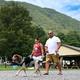 Ground-level scene showing guests walking a dog with campground pavilion and RVs in background — conveys family-friendly atmosphere and site amenities referenced on the homepage.