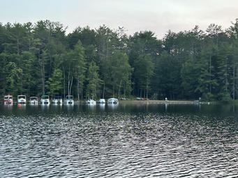 Shoreline with multiple boats moored at docks across the pond — depicts the camp’s boat docks and waterfront facilities (from the ‘Around the Camp’ page).