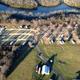 High-resolution aerial photograph showing the campground layout: rows of RV sites, access roads, central pavilion/buildings and adjacent river/wooded boundary. Image is hosted on the property homepage and clearly depicts on-site RV pitches and grounds.
