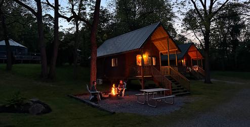 Cabins at dusk with lit porch, picnic table and fire pit — good representation of the park’s cabin lodging and campsite ambiance (used on site slide for cabins).