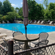 Empty outdoor swimming pool surrounded by lounge chairs and green trees on a sunny day.
