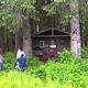 Three people outside brown cabin with trees and ferns