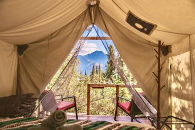 View from inside a tent framing distant mountains — useful interior-to-exterior shot demonstrating tent layout, bed setup and the scenic mountain views offered on-site (used on property pages).