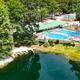 Drone/oblique view focused on the pond, pool complex and docks with kayaks — highlights amenities and waterfront features on the campground grounds.