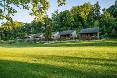 Landscape view of a row of cabins with grassy foreground and wooded backdrop — illustrates the property’s cabin accommodations (from the cabins page).
