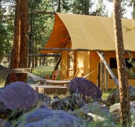 Glamping tent pitched in a treed meadow — shows the resort’s canvas glamping accommodations and immediate surroundings (deck, hammock), matching the property’s glamping offering on the website.