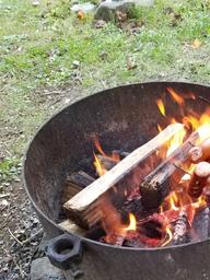 Close-up photo of a metal fire ring with burning wood and cooking—useful detail of campsite amenities (fire pit). Image appears on the campground’s gallery pages on the site.