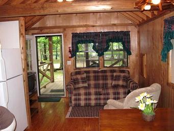 Interior view of a cabin living area (sofa, kitchenette, entry to porch) — useful for showing accommodation interior for the campground’s cottage/cabin rentals.