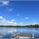 A wooden dock overlooking a calm lake under a blue sky with scattered clouds.
