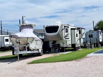A fifth wheel and a covered boat on its trailer parked side by side at one site