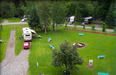 Ground-level aerial/overview of central grassy area with benches and a fire ring, showing campground communal space and nearby RVs (Photos_700x462_g2).