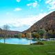 Wide landscape shot of the pond with surrounding campsites and trailers, valley hills in background — good scenic overview used on the campground gallery (Frank Serio photo on site).