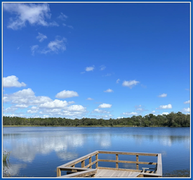 A wooden dock overlooking a calm lake under a blue sky with scattered clouds.