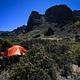 tall cliffs overlook tent site with orange tent and one camper