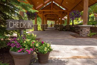 Covered check-in walkway with hanging planters and signage; shows guest arrival area and building materials/landscaping on the property (homepage background image).