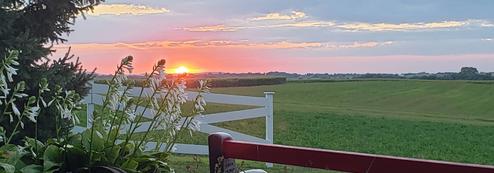 Sunset vista over open fields with white fence and part of a porch visible — illustrates scenic grounds and rural setting on the property page.
