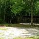 Trees shadow over gravel parking pad with picnic table nearby