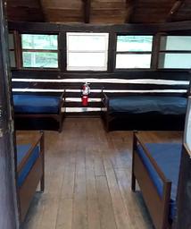 Interior of cabin from front door.  Wooden floor with 4 metal cots and vinyl covered mattresses.