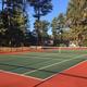 Clear photograph of a full-size outdoor tennis court framed by trees, showing on-site sports facilities and site landscaping; from the campground’s photo gallery page.