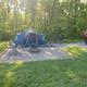 Tent campsite on a gravel pad with fire ring, picnic table and wooded backdrop — shows a typical tent pitch available at the campground (from waystostay photos on the site).