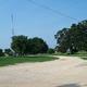 Wide view of the park grounds showing gravel roads, open turf, large shade trees and RVs/campsites in the distance — a good overview of Sonny’s RV Park layout (image used on the property home page).