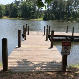 Wooden fishing dock extending into the lake with shoreline and 'no swimming' sign — clearly shows on-site waterfront amenity referenced on the park website. Good facility/detail shot.