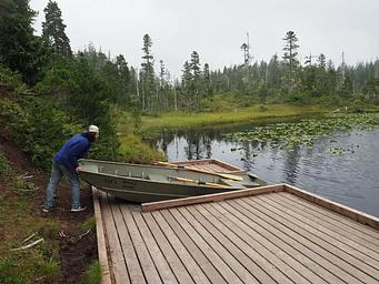 Person pushing skiff into lake from platform
