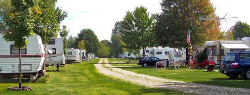 Panoramic view of an RV row with parked trailers, gravel drive and grassy sites — useful for illustrating full-hookup/RV camping areas. Image is from the site (RV Row-033.jpg) and appears on the campground's pages.