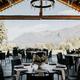 Outdoor dining area with round tables, set for an event. Features wooden beams and mountain views. Elegant and scenic setup for gatherings.