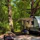 Well-lit campsite scene with travel trailer, picnic table and fire ring — good close view of a campsite setup and facilities (tables, level pad). Image is on the campground page.
