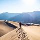 Person walking the ridge of a sand dune, leaving footprints in the sand.