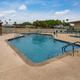 Ground-level pool photograph showing pool shape, lounge chairs and adjacent buildings — useful detail shot of main recreational facility from the property listing.